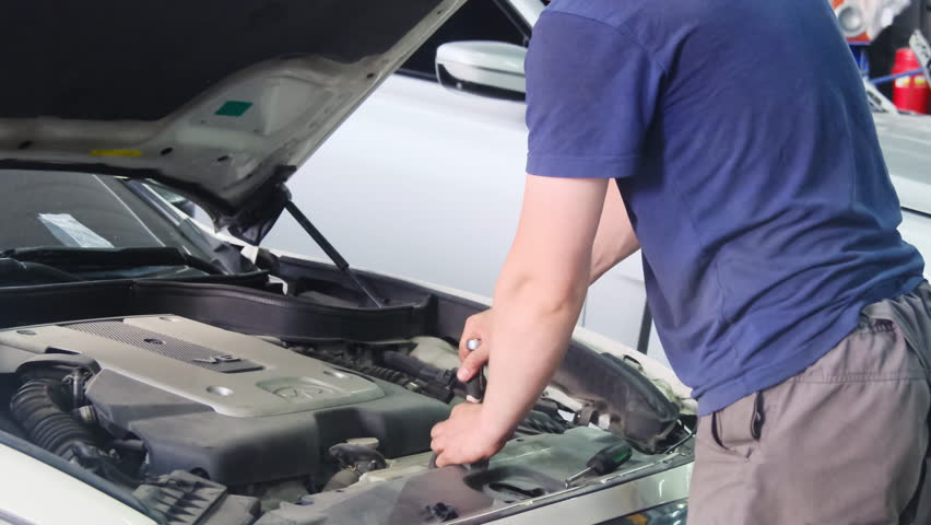 Mechanic unscrews nut on vehicle engine unit in repair shop closeup. Professional worker fixes car motor with manual tools at service station