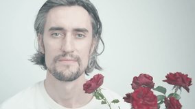 Contemplative Young Man with Long Tousled Hair and Beard Sitting Against Minimalistic White and Gray Background with Red Roses - Powered by Shutterstock - Get 15% off with code: PIKWIZARD15