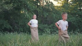 Boy leads sack race outdoors. Girl behind tries to catch up in jumping game. Summer fun for children. Boy jumps with focus. Active kid enjoys competition. Nature game with girl and boy child. - Powered by Shutterstock - Get 15% off with code: PIKWIZARD15