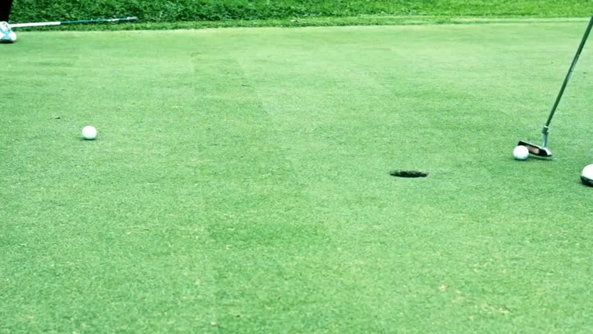 Golfer takes a smooth putt, ball rolling on vibrant green grass towards the hole. Excellent portrayal of precision and focus on golf course.