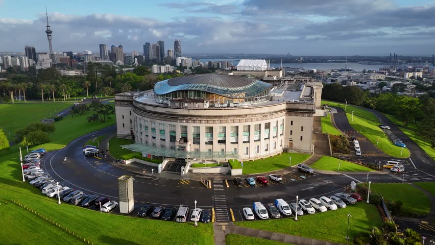 Aerial view of the Auckland War Memorial Museum, its curved facade contrasting with the sharp lines of the city skyline in the background, Auckland, Auckland, New Zealand.