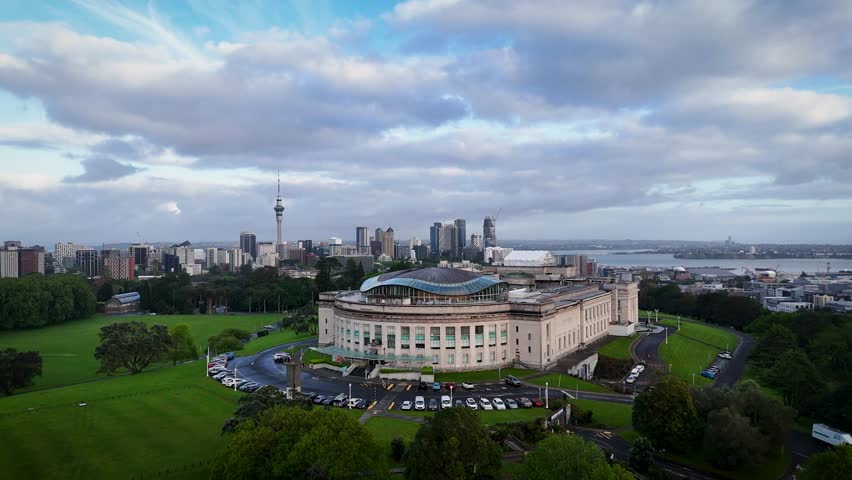 Aerial view of the Auckland War Memorial Museum stands majestically amidst lush green parkland, contrasting with the city skyline and cloudy skies, Auckland, Auckland, New Zealand.