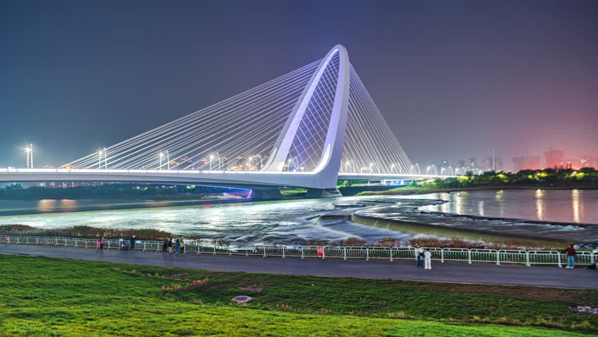 Citizens walking at night on the green grass near the Shougang Bridge over the Yongding River in Shijingshan, Beijing, China