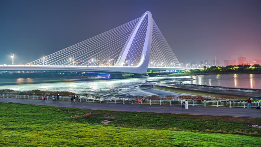 Citizens walking at night on the green grass near the Shougang Bridge over the Yongding River in Shijingshan, Beijing, China