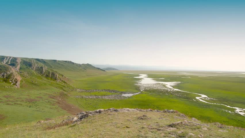 Expansive grassland landscape with winding streams under a clear blue sky view