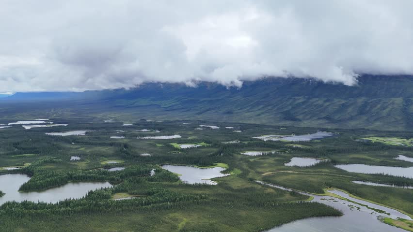 Breathtaking Alaskan landscape with many lakes surrounded by lush greenery and distant mountains shrouded in mist creates a serene natural panorama