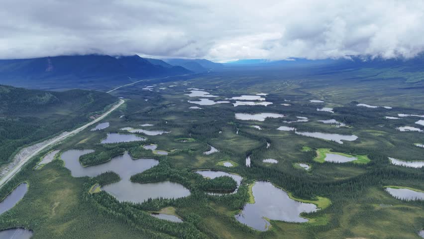 Dramatic aerial footage reveals Alaskan landscape with lakes and mountains under cloudy skies, perfect for travel documentaries and nature explorations