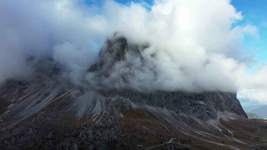 Aerial view of a majestic mountain peak shrouded in ethereal clouds, contrasting with the rugged terrain below, Trentino-South Tyrol, Italy.