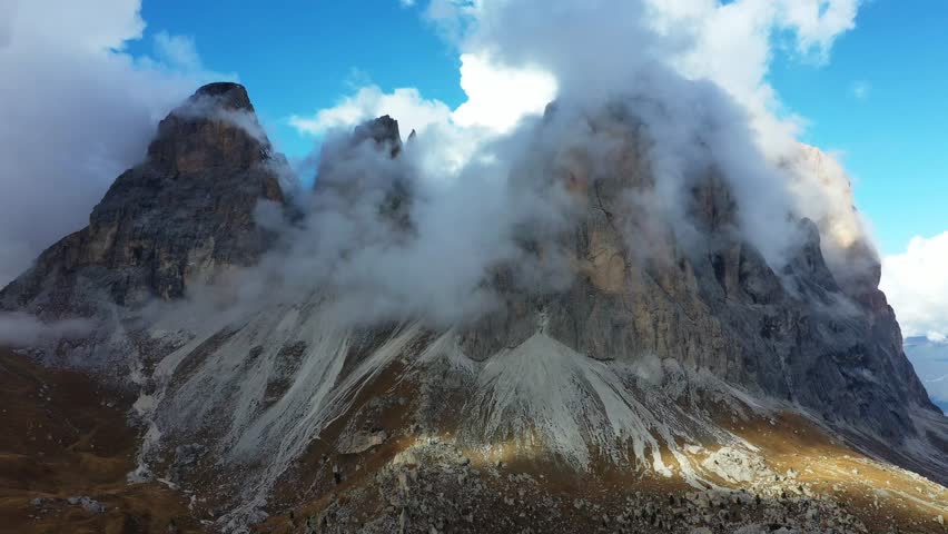 Aerial view of rugged, rocky mountains piercing through a sea of clouds, creating a stunning contrast against the clear blue sky, Trentino-South Tyrol, Italy.