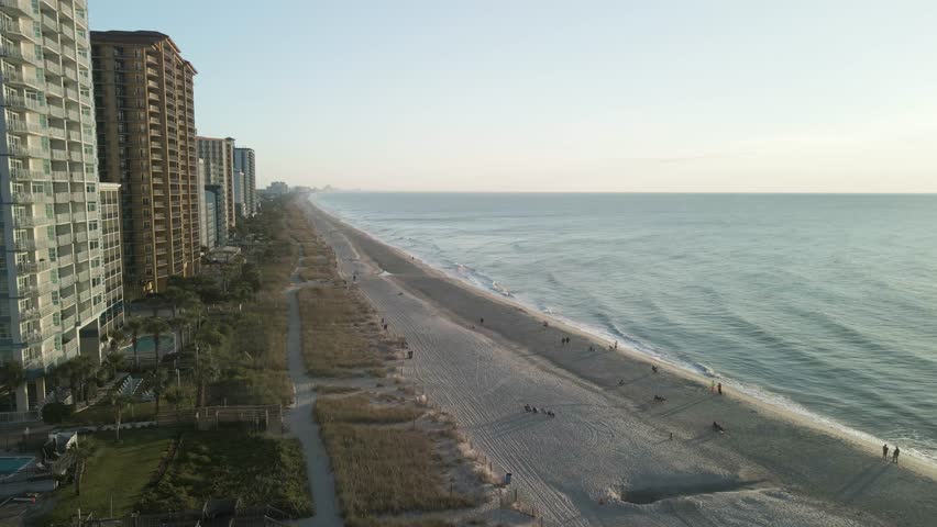 Aerial drone flying towards coastal buildings along Myrtle Beach, South Carolina, during sunrise golden hour.