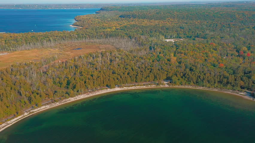 The shoreline of Door County, Wisconsin, curves around a calm green bay bordered by dense autumn forest, where warm fall colors meet the blue expanse of Lake Michigan.