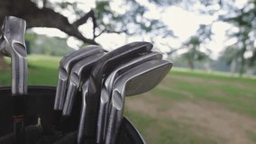 Close-up of golf clubs positioned in a bag, set against a scenic view of a golf course with trees and open grassy areas in background. - Powered by Shutterstock - Get 15% off with code: PIKWIZARD15