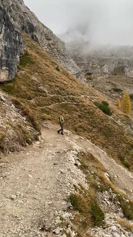 Female hiker with trekking poles and dog walking on rocky mountain trail in Dolomites