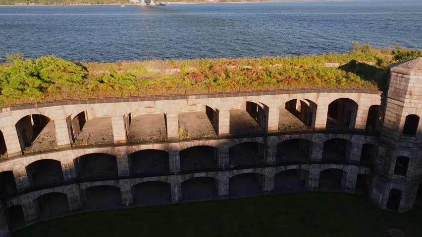 Close-up aerial view of Battery Weed historic fort in Staten Island, New York, showing detailed stone walls, arched passages, and greenery on top under clear blue sky. ProRes HQ422.