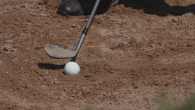 Golfer prepares to strike a white ball nestled in sand, demonstrating a swing technique for a challenging bunker shot amidst a sunny outdoor setting. - Powered by Shutterstock - Get 15% off with code: PIKWIZARD15