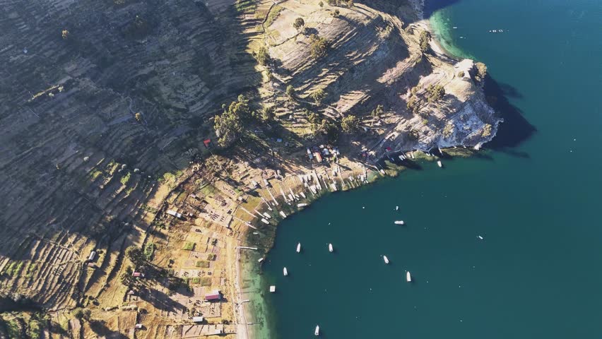 Smooth aerial pan from boats in the harbor of Isla del Sol across the island to the horizon on Lake Titicaca, Bolivia. Sunny day with blue sky and calm water.