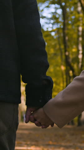 Vertical cropped shot of loving couple holding hands together while strolling along path in autumn park