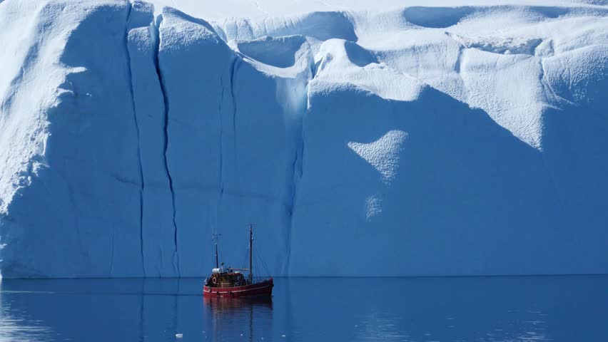 Small fishing boat sailing near a massive iceberg in the arctic waters of Greenland
