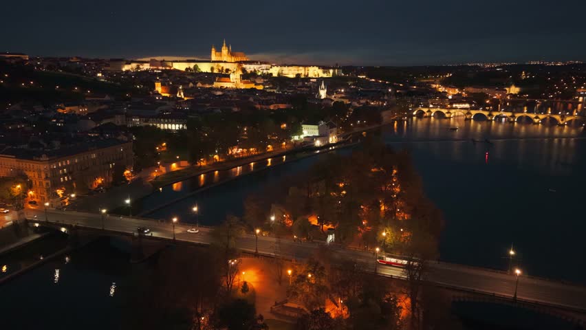 Aerial night view of Prague Castle, Charles Bridge, and Střelecký Island with tram crossing the illuminated riverside streets along the Vltava River in the historic heart of Prague, Czech Republic.