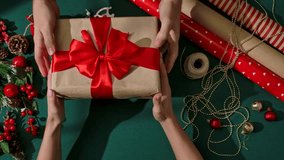 Top view of two people exchanging Christmas gifts wrapped in craft paper and tied with a red bow on a green background, symbolizing the festive atmosphere and warmth of the holiday. - Powered by Shutterstock - Get 15% off with code: PIKWIZARD15