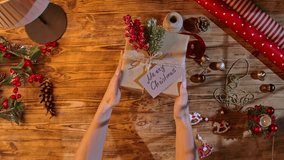 Top view of two people exchanging Christmas gifts wrapped in craft paper and tied with twine, pine cones, and red berries on a wooden table, symbolizing the festive atmosphere and warmth of the - Powered by Shutterstock - Get 15% off with code: PIKWIZARD15