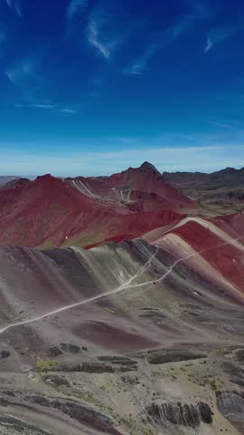 A vertical drone shot above the colorful Rainbow Mountain in Peru, revealing stunning natural mineral layers and rugged Andean terrain under clear sky