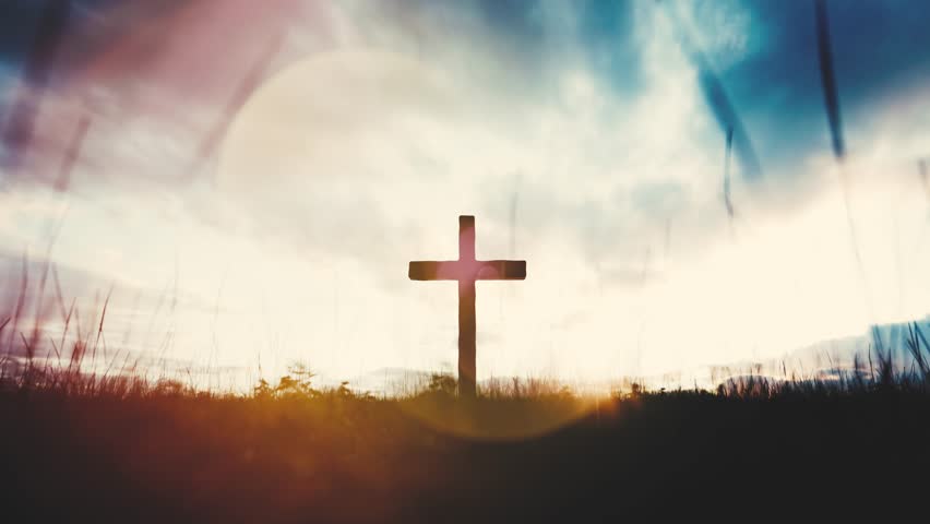 Wooden cross standing on a hill at sunset with moving clouds and light leaks. Religion and faith