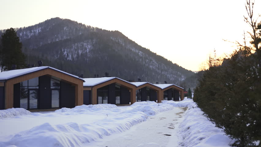Wooden cabins on snowy road side at winter glamping in forest. Comfortable cottages attract tourist to spend holiday at ski resort