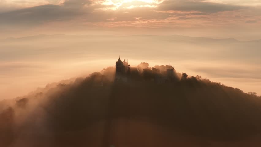 A straight-down drone view of Hrad Doubravka veiled in early morning fog, with its stone ruins barely piercing the dense cloud layer above the trees