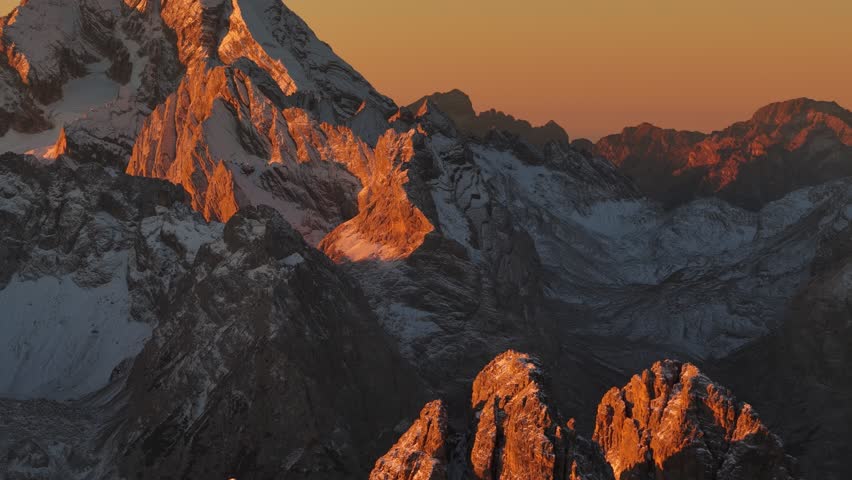 Warm, dramatic sunlight striking the rugged Cadini di Misurina rock towers during a vivid sunset, snow and red-orange skies in the Dolomites