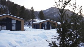 Modern wooden cabins with glass facades in snowy yard at winter glamping. Cozy cottages against hills covered with pine woods at sunrise - Powered by Shutterstock - Get 15% off with code: PIKWIZARD15