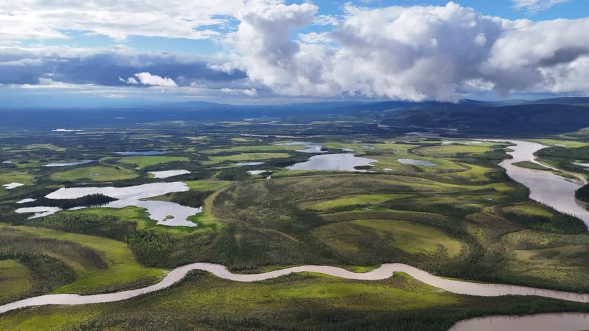 Dramatic aerial view of meandering river flowing through lush green landscape under dynamic cloudy sky in Alaska, perfect for travel inspiration and outdoor adventure content