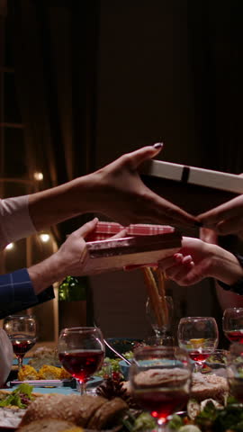 Vertical slow motion video hands exchanging christmas gifts above festive table cozy light warm home atmosphere concept friendship gratitude joy holiday celebration winter evening