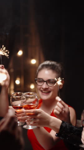 Vertical cinematic slow motion video joyful friends raising glasses with sparklers at festive dinner table cozy warm light holiday atmosphere concept friendship celebration christmas new year