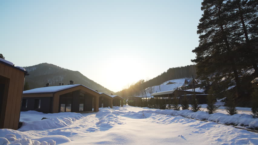 Cozy tourist cabins on snowy road side at eco glamping. Comfortable cottages of wood in small mountain resort village. Winter vacation