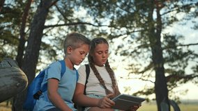 Children sit in forest using tablet together. Girl and boy explore screen sitting on log. Device in hands outdoors nature. Children tablet smile forest. Sibling use device tablet in forest sitting. - Powered by Shutterstock - Get 15% off with code: PIKWIZARD15