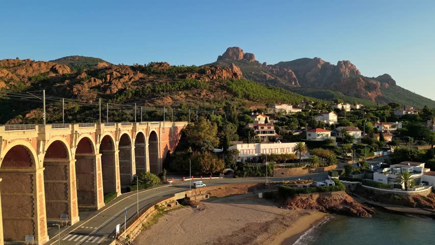 Aerial cinematic view of a train crossing the Antheor Viaduct in the Esterel Mountains near Saint Raphael, French Riviera, overlooking the Mediterranean Sea and luxury villas along the Cote dAzur at s