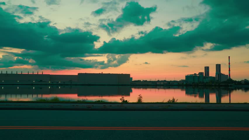 Industrial paper mill at sunset in Wisconsin Rapids, reflecting in calm water under moody clouds. Cinematic time-lapse day to night.