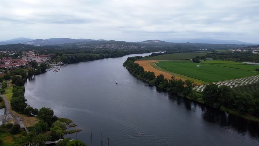 4K drone aerial shot of the Minho River, forming the natural border between Spain and Portugal near the historic town of Tui, Galicia, on a cloudy day.