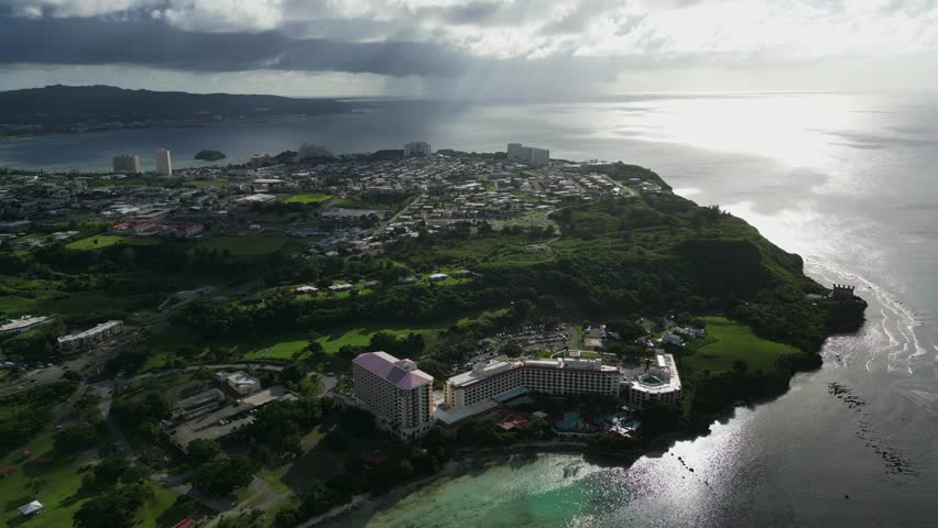 Idyllic orbiting aerial view of coastal resort, hotels, and scenic spots at Oka, Tamuning, Guam during sunset.