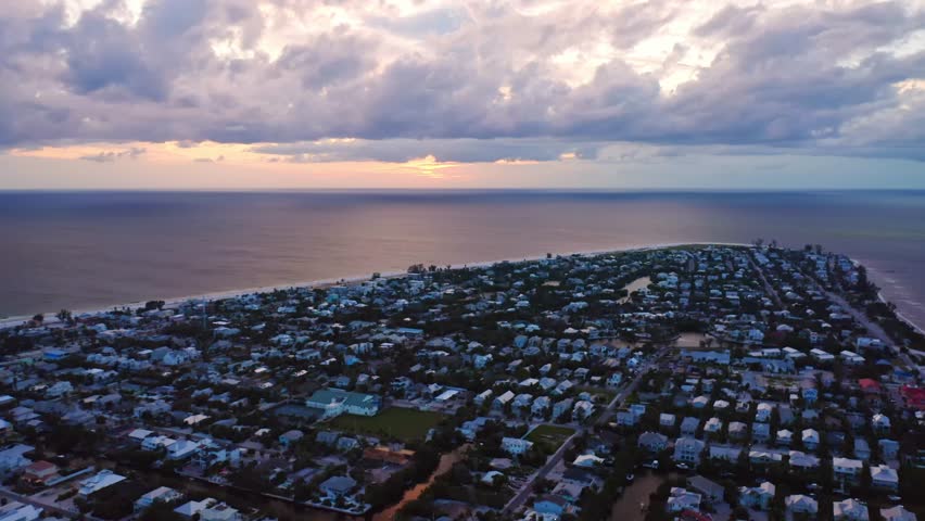 As twilight settles over Anna Maria Island, pastel homes and winding streets glow beneath streaked clouds, while the Gulf horizon fades into a golden-blue evening calm.