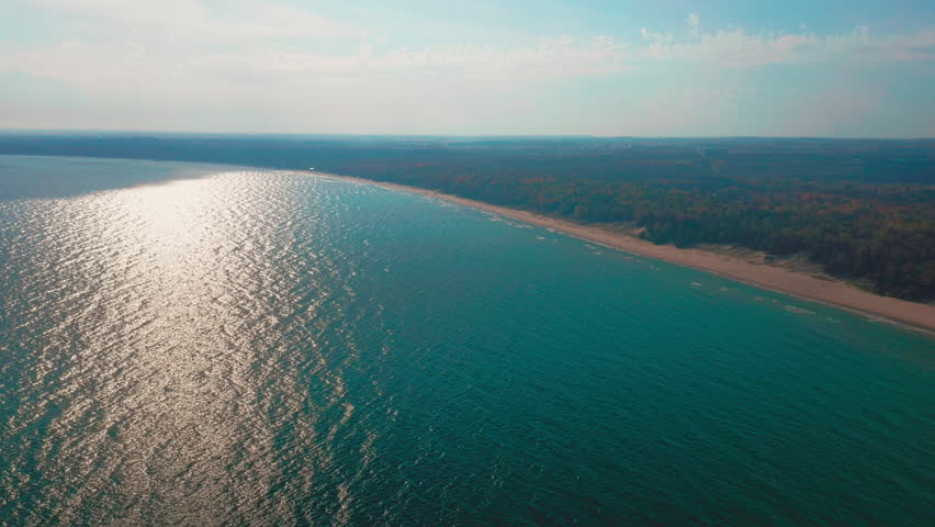 The afternoon sun shimmers across Lake Michigan’s turquoise surface as it meets the sandy shoreline of Door County, creating a tranquil and expansive aerial view of natural beauty.