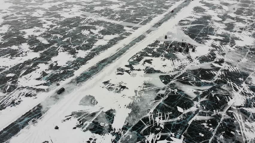Cars drive on the ice of Lake Baikal to Olkhon Island, aerial view. Winter trip.