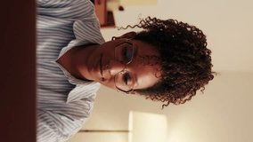 Vertical video,Focused young woman working from home on her laptop. She's wearing glasses and a striped shirt and looks thoughtful while working. - Powered by Shutterstock - Get 15% off with code: PIKWIZARD15