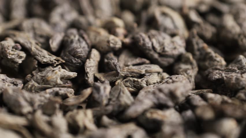 Green dried gunpowder chinese tea leaves with scoop on white wooden background, closeup.