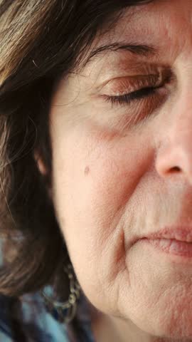 Vertical close-up shot of an elderly woman's half face, capturing the lines and emotions etched into her skin. The detailed focus highlights her life experiences and the wisdom in her eyes
