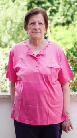 Vertical medium shot of an elderly woman with short red hair looking seriously at the camera. Her intense gaze and serious expression convey a sense of determination and strength