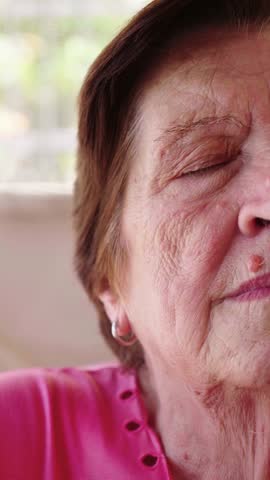 Vertical close-up shot of an elderly woman with short red hair, capturing half of her face. Her expression is deeply emotional, revealing a depth of feelings and life experiences etched