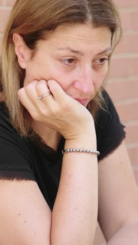 Vertical shot of a young woman with long blonde hair, sitting at a table and looking visibly sad. Her expression reflects the impact of receiving bad news, capturing a moment of emotional distress