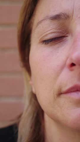 Vertical close-up shot of a young woman with long blonde hair, capturing half of her face. Her expression is deeply emotional, revealing a depth of feelings and life experiences etched